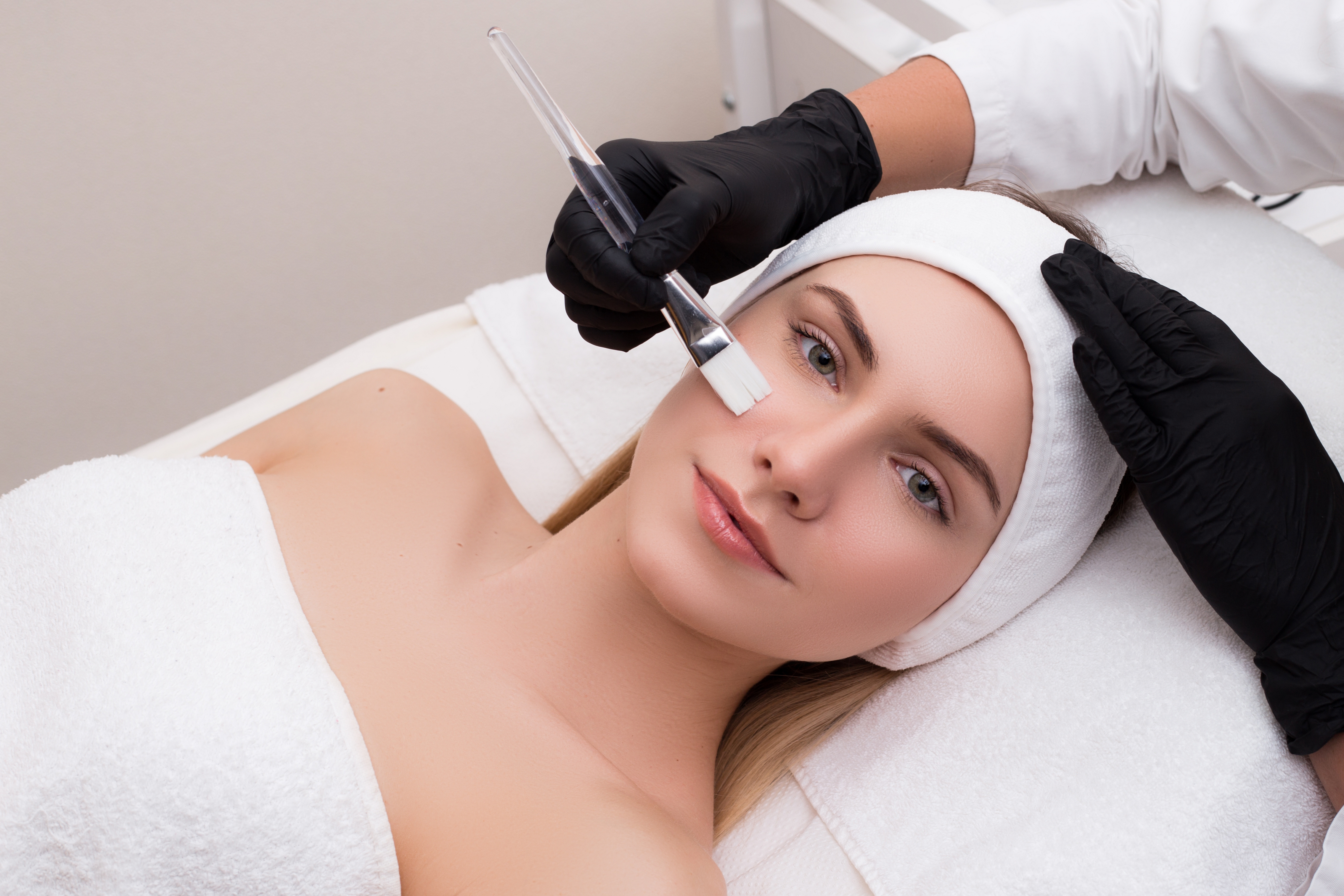 Take care of your skin! Attractive young lady lying on the table getting a facial mask as the cosmetology procedure in a salon.